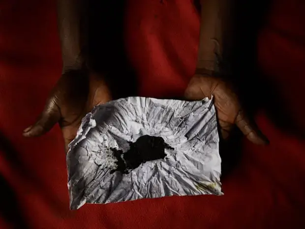 Blandine Yoyani, a traditional healer in Mbandaka, shows her remedy for snakebites. Herbs and a snake head are ground into powder then burned before being rubbed into a small razor cuts made on the arms of a snakebite victim. Image by Hugh Kinsella Cunningham. Congo, 2019.