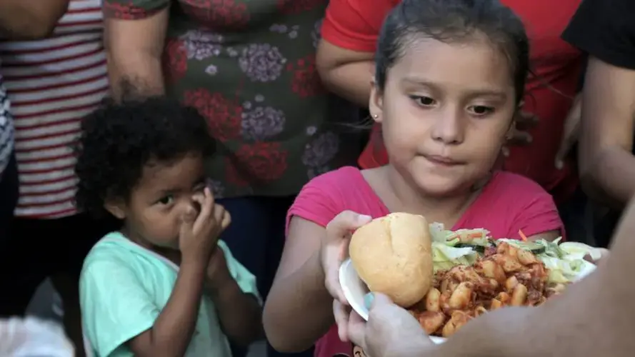 Migrant children line up for food at a migrant camp on the Matamoros, Mexico, side of the Gateway International Bridge that connects Matamoros to Brownsville, Texas. Image by Jose A. Iglesias. Mexico, 2019.