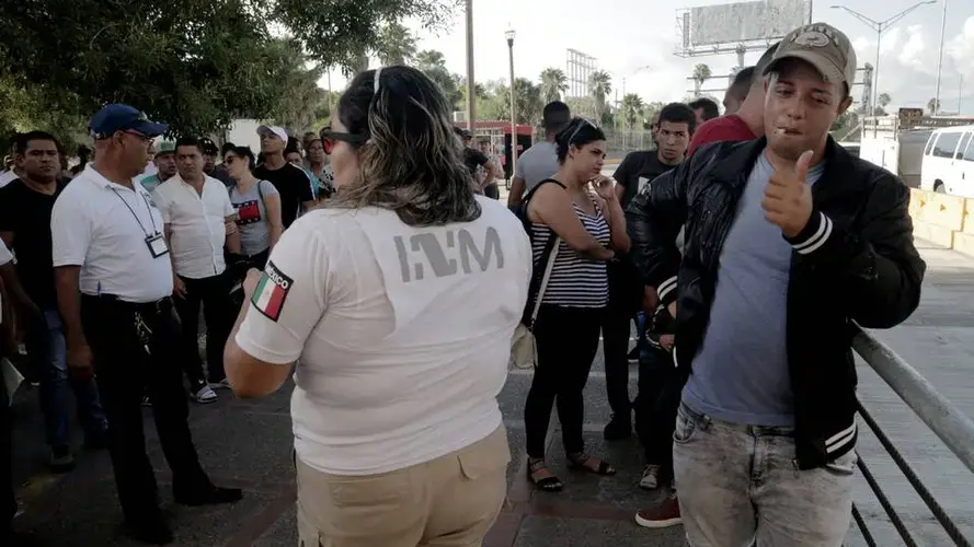 Ronald Sicilia Espinosa, a Cuban migrant, right, gives the thumbs up to well-wishers after being the first number called to cross into the United States to ask for asylum. Sicilia was happy that his turn finally came. after he had waited over two months for his number to be called. Image by Jose A. Iglesias. Mexico, 2019.