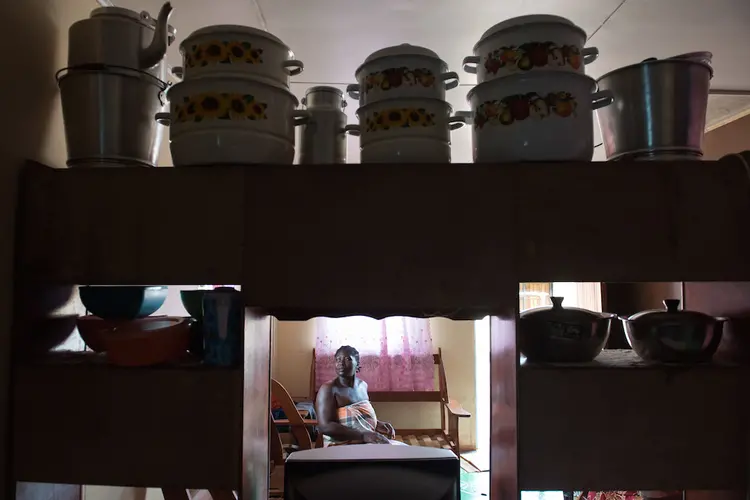 Marta Prika sits in her home in Adjuma Kondre. The paneling on the wall behind her was provided by Alcoa subsidiary Suralco after the village pleaded and protested the company's bauxite mining in the jungle surrounding their homes, gardens, rivers, and swimming holes. The paneling is not the kind commonly used in the region and is slowly being eaten away by termites—a cosmetic gesture that adds to local resentment as issues like clean water remain unaddressed. Image by Stephanie Strasburg. Suriname, 2017.