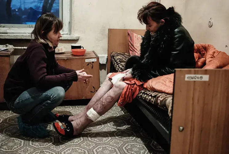 Roza, left, an outreach worker with Club Svitanok, kneels in 2011 across from Katya, 37, who is HIV-positive and struggling with drug addiction, in a Donetsk hospital where she was being treated for pneumonia. Image by Misha Friedman. Ukraine, 2011.