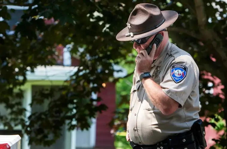 A deputy with the Lincoln County Sheriff's Office takes a phone call outside the scene of an investigation in Boothbay Harbor in this 2015 file photo. Image by Ashley L. Conti/BDN. United States, 2015.<br />
