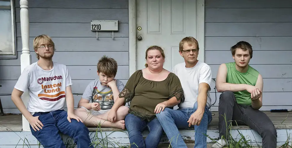 The Myers family sits on the porch of their rental home in Tulsa, Oklahoma. The new federal eviction moratorium will allow them to stay there through the end of the year. But health problems for both Jack and Beth Myers mean the future is uncertain for the family of six, including, from left, Duncan, 21, Riley, 9, parents Beth and Jack, and Dylan, 20. Image by Mike Simons. United States, 2020.