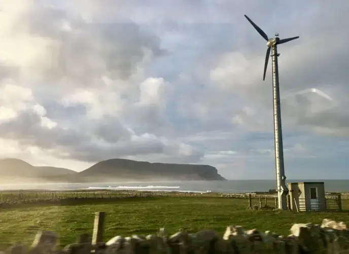 A wind turbine on a farm on the Orkney mainland faces one of the smaller islands off the coast. Image by Maggie More. United Kingdom, 2020.