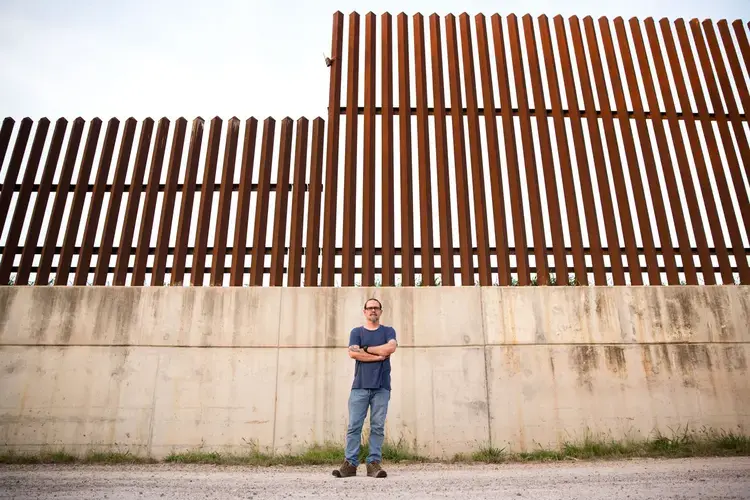Scott Nicol, co-chair of the Sierra Club’s Borderlands Campaign, stands in front of a concrete levee topped by the border fence in Hidalgo County. Environmentalists, along with the U.S. Fish and Wildlife Service, say the barrier endangers wildlife because animals can't reach dry land during floods. Image by Callie Richmond. United States, 2017.