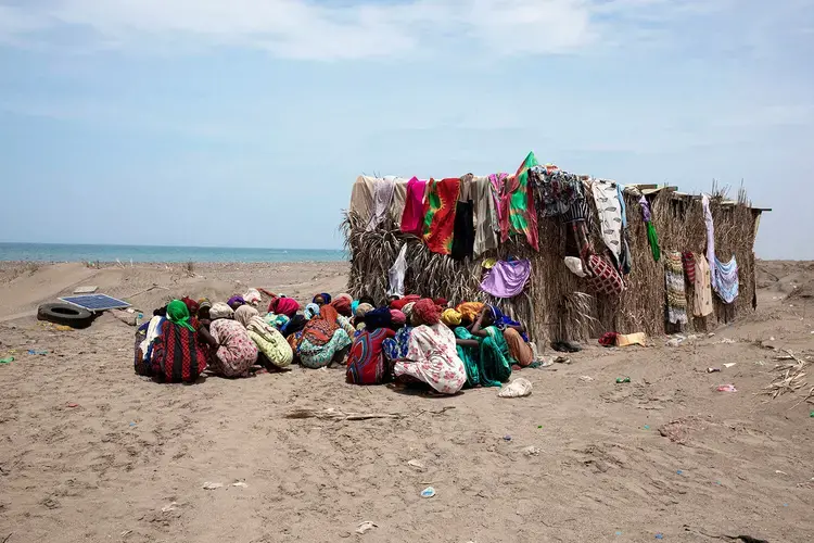 In this July 26, 2019 photo, Ethiopian migrant girls eat outside their lockup known in Arabic as a 'hosh,' in Ras al-Ara, Lahj, Yemen. Some lockups hold as many as 50 women at a time. The women will stay here for several days until their transportation is ready. Image by Nariman El-Mofty / AP Photo. Yemen, 2019.