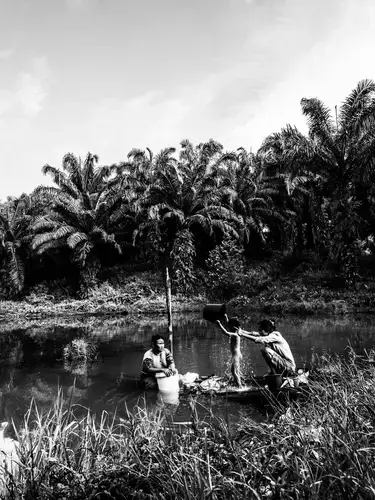 Ida and a neighbor bathe Ida’s daughter Santi in the murky water near their home. Image by Xyza Cruz Bacani. Indonesia, 2018.