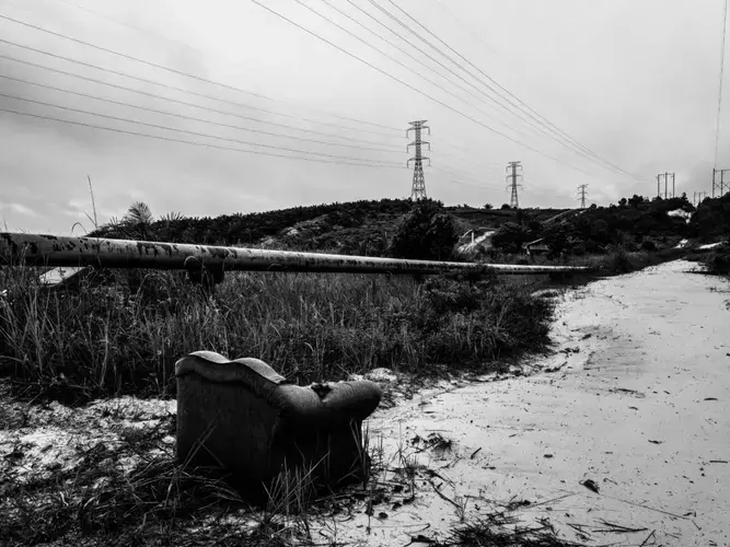 An abandoned sofa sits near the oil pipeline in Kandis. Miles of crude oil and gas pipeline and hectares of palm trees run alongside a road in Kandis, Riau, Indonesia on June 27, 2018. Image by Xyza Cruz Bacani. Indonesia, 2018.