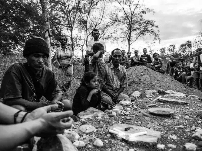 Mikhael and his grandchildren, together with other villagers, pray at a makeshift grave for Dolfina. Image by Xyza Bacani. Indonesia, 2018.
