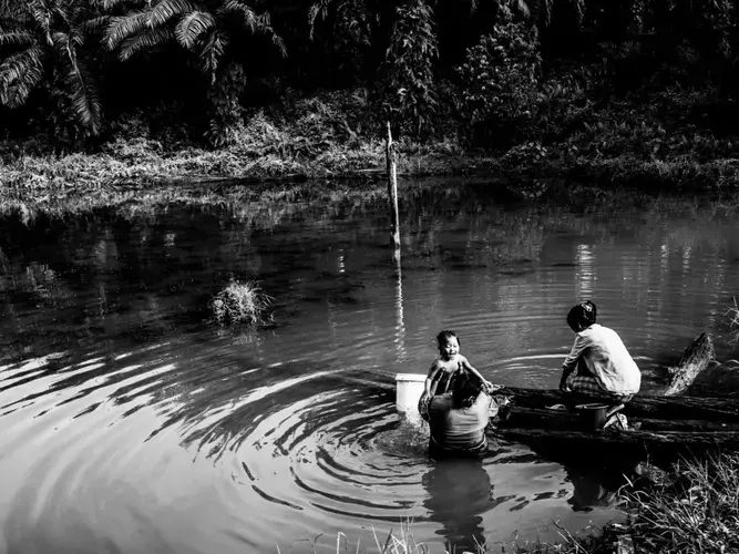 Santi takes a bath in the murky water with a neighbor while her mother Ida washes their clothes. The reservoir is the community only source of water. Image by Xyza Cruz Bacani. Indonesia, 2018.