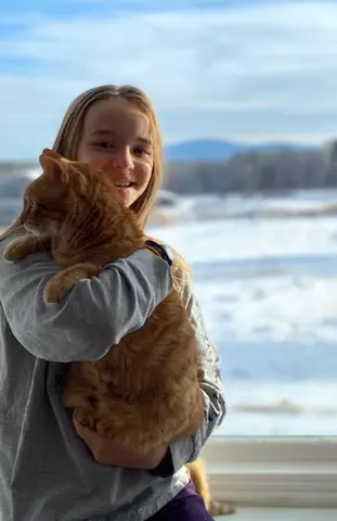Headshot for Chloe Carrdus holding a cat. A beach and waves are in the background.
