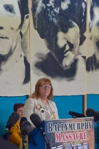 A woman stands at a podium in front of a black and white mural.