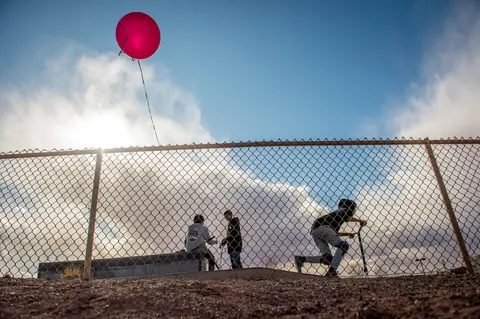 Children play behind a chain-link fence in Tuba City. Image by Mary F. Calvert. United States, 2020.