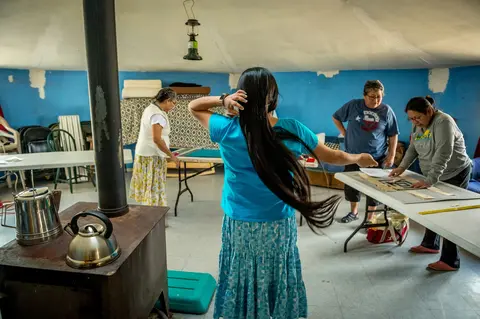 Tara Begay fixes her hair while sisters Carol Talker, Leona Begishie and Linda Talker, work on a quilt in their family hogan (traditional Navajo house) in Cameron, Ariz. Image by Mary F. Calvert. United States, 2020.
