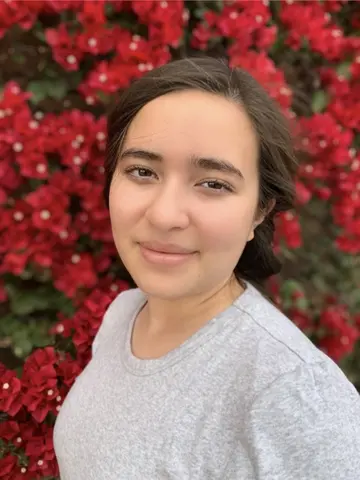 Headshot for Carolina Leon. In the background, there are red flowers.