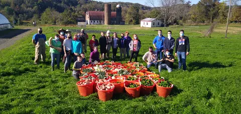 A group of people pose outdoors for a photograph with baskets of produce in front of them.