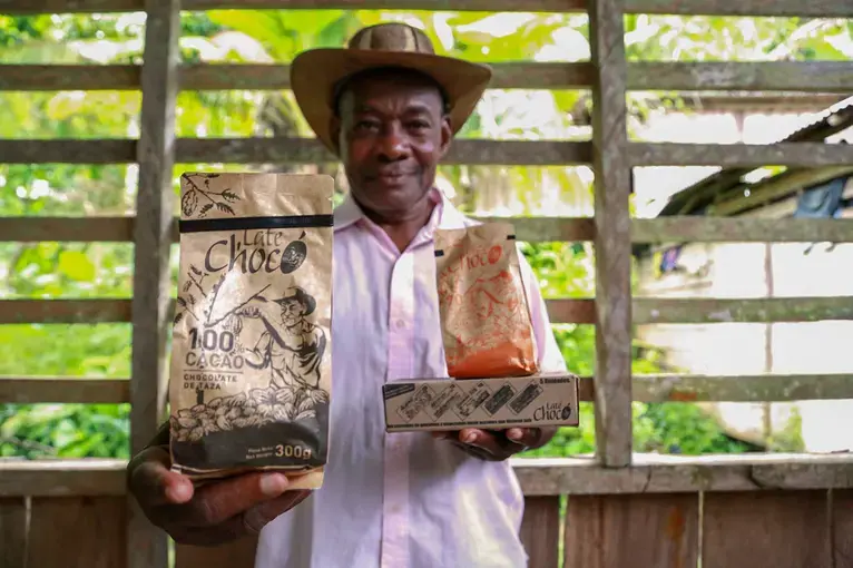 José Palacios, a cacao farmer, holds the Late Chocó chocolate products produced by his son, Joel, in Bogotá. The package bears an illustration of his likeness. José Palacios lives in Colombia's western Chocó department, which is also a coca-growing region. Image by Verónica Zaragovia. Colombia, 2018.