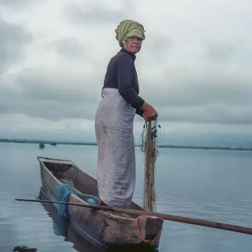 Moirang Themapabi, 60. Thanga Tongbram Leikai, Manipur Moirang Themapabi has been fishing in Loktak Lake and selling her catch since she was a teenager. The construction of the Ithai Dam has resulted in fish scarcity in the lake, impacting the livelihood of her entire family. She spends more hours fishing than she did before the dam was constructed. Over the years due to long working hours, she has developed severe calf and backache issues.