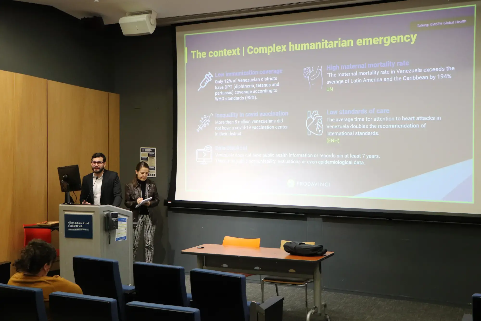 Man and woman stand at podium in front of screen.