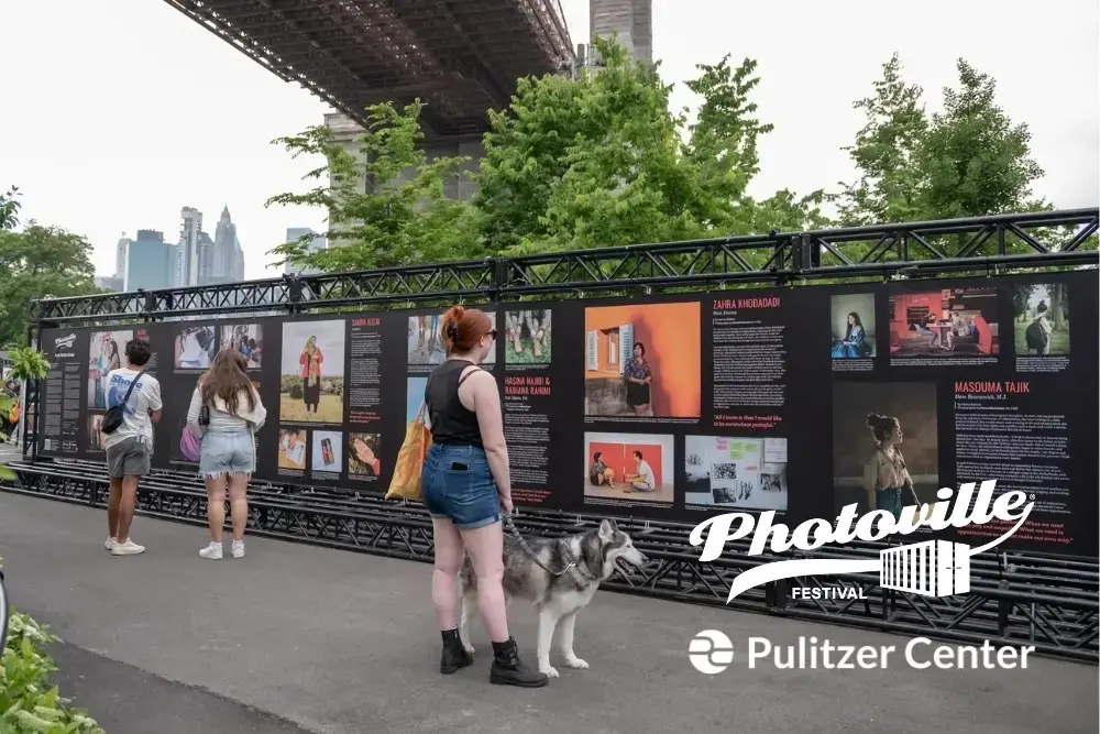 people look at a photography exhibit under the Brooklyn Bridge at Photoville Festival