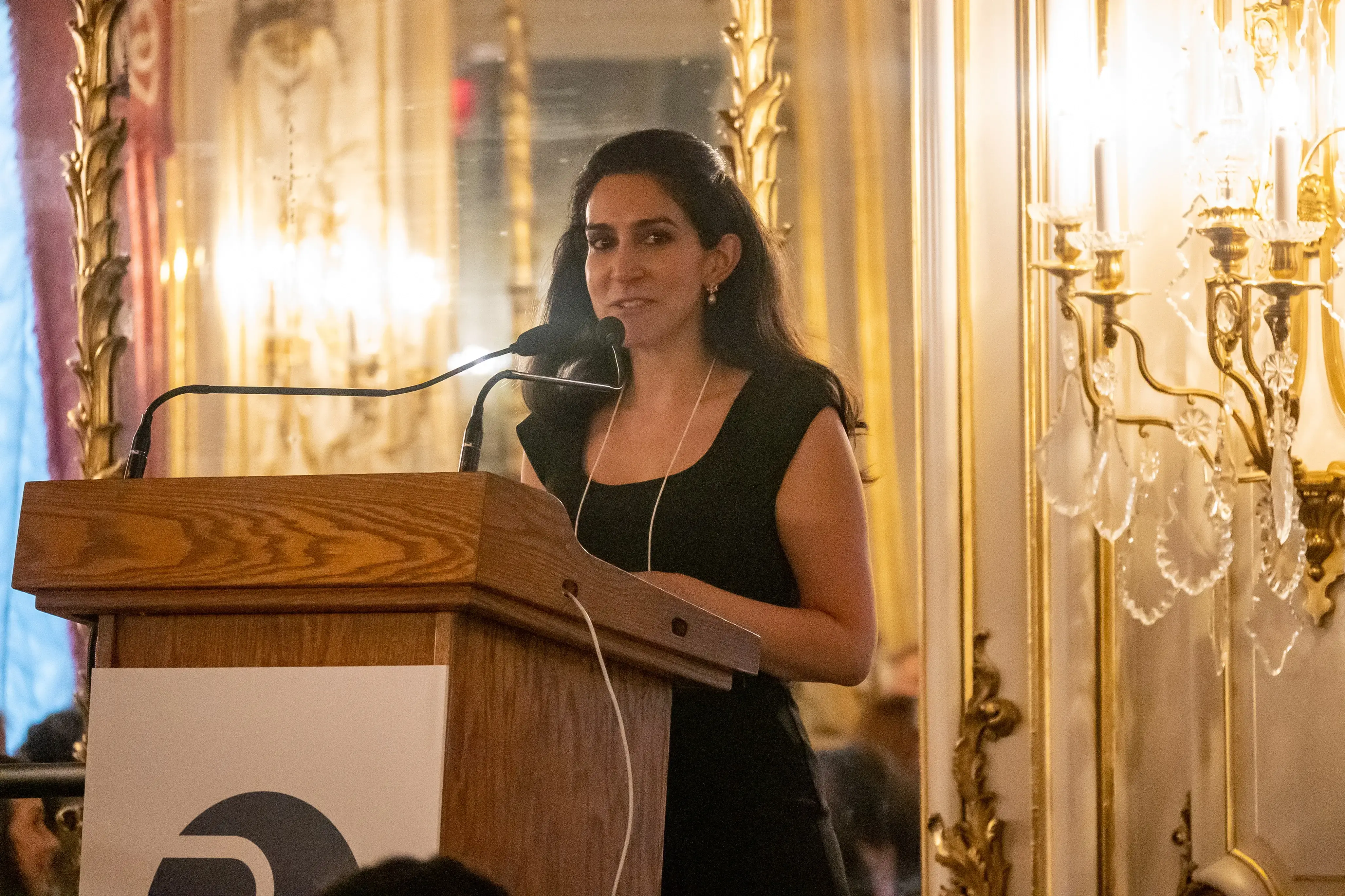Azmat Khan stands at a podium to speak at the ornate Cosmos Club event salon.