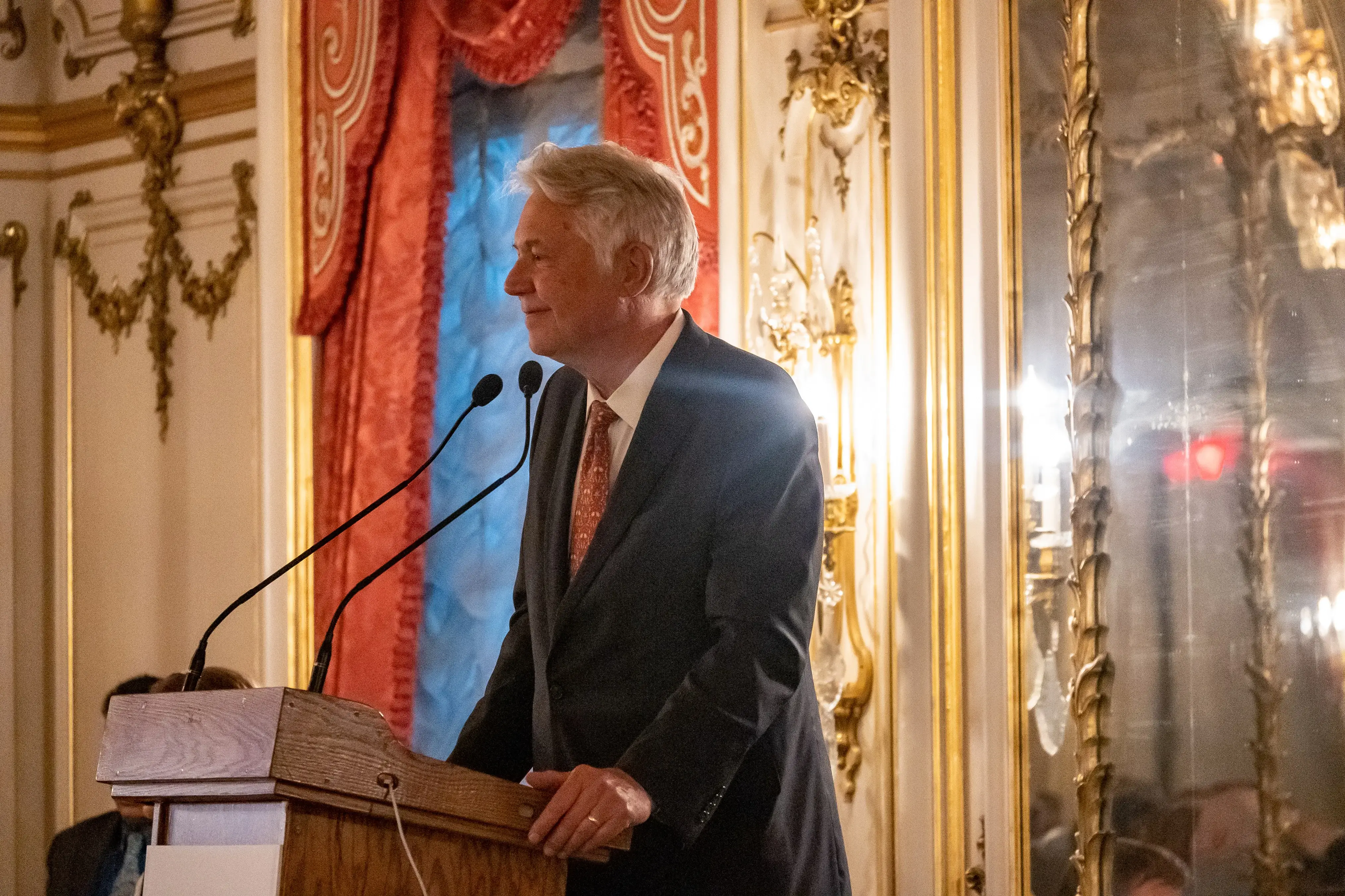 Jon Sawyer speaks at the podium of the ornate Cosmos Club event salon.