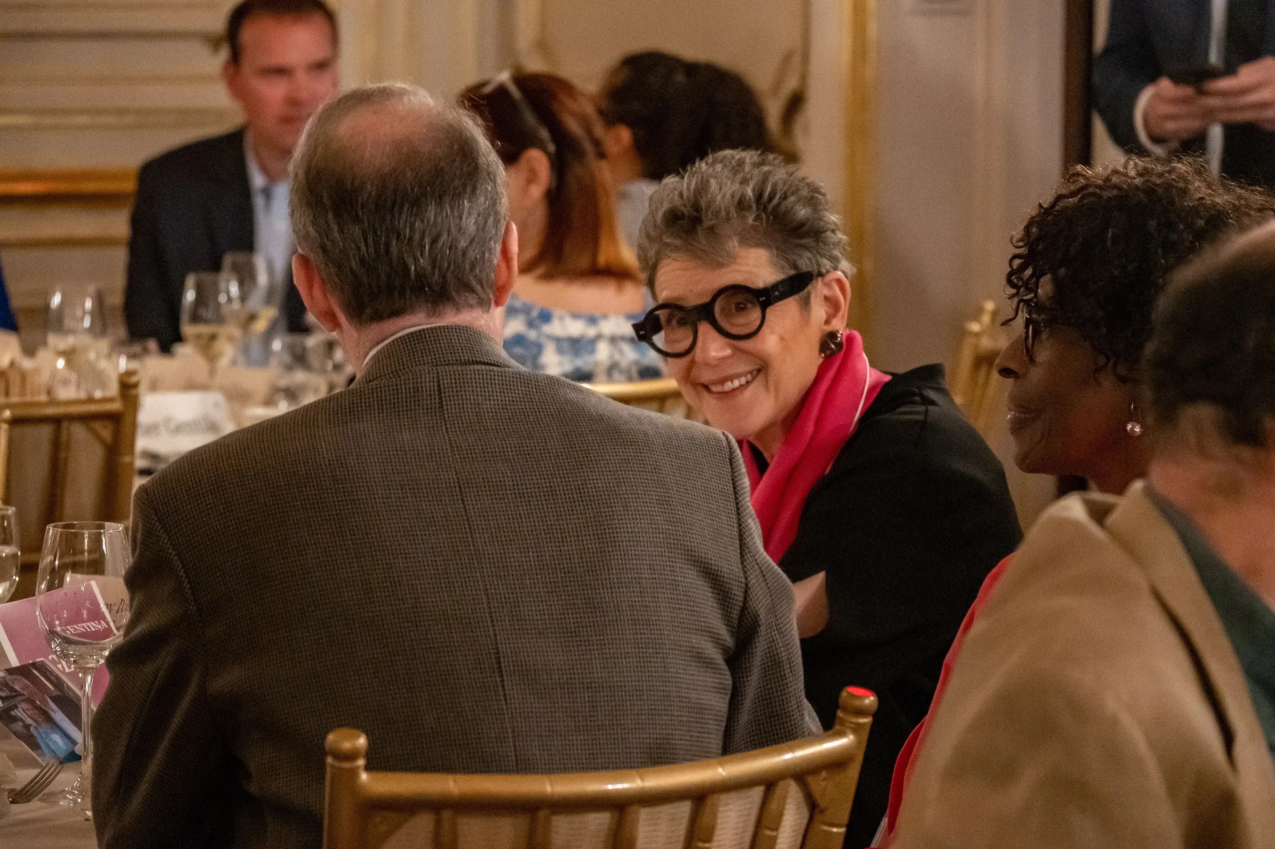 Board member Tracy Riese speaks with fellow members at a dinner table at the ornate Cosmos Club event salon.