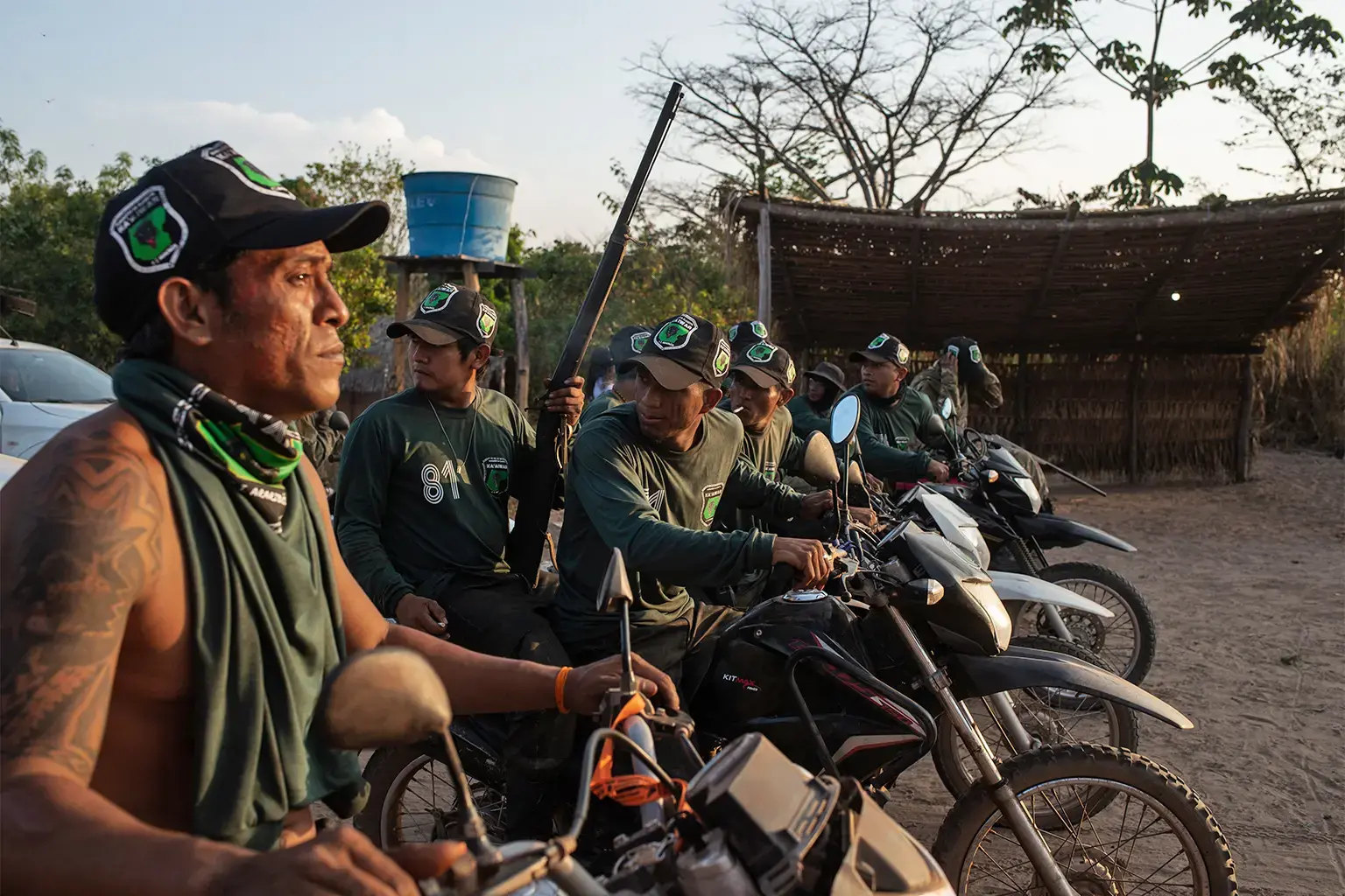 Several men sit on motorcycles, facing the sun.