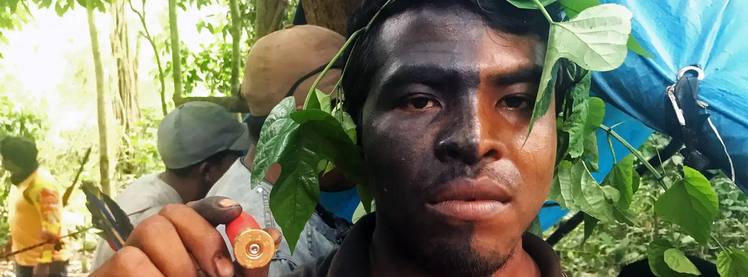 A man with half of his face stained black holds up a buck shot casing.