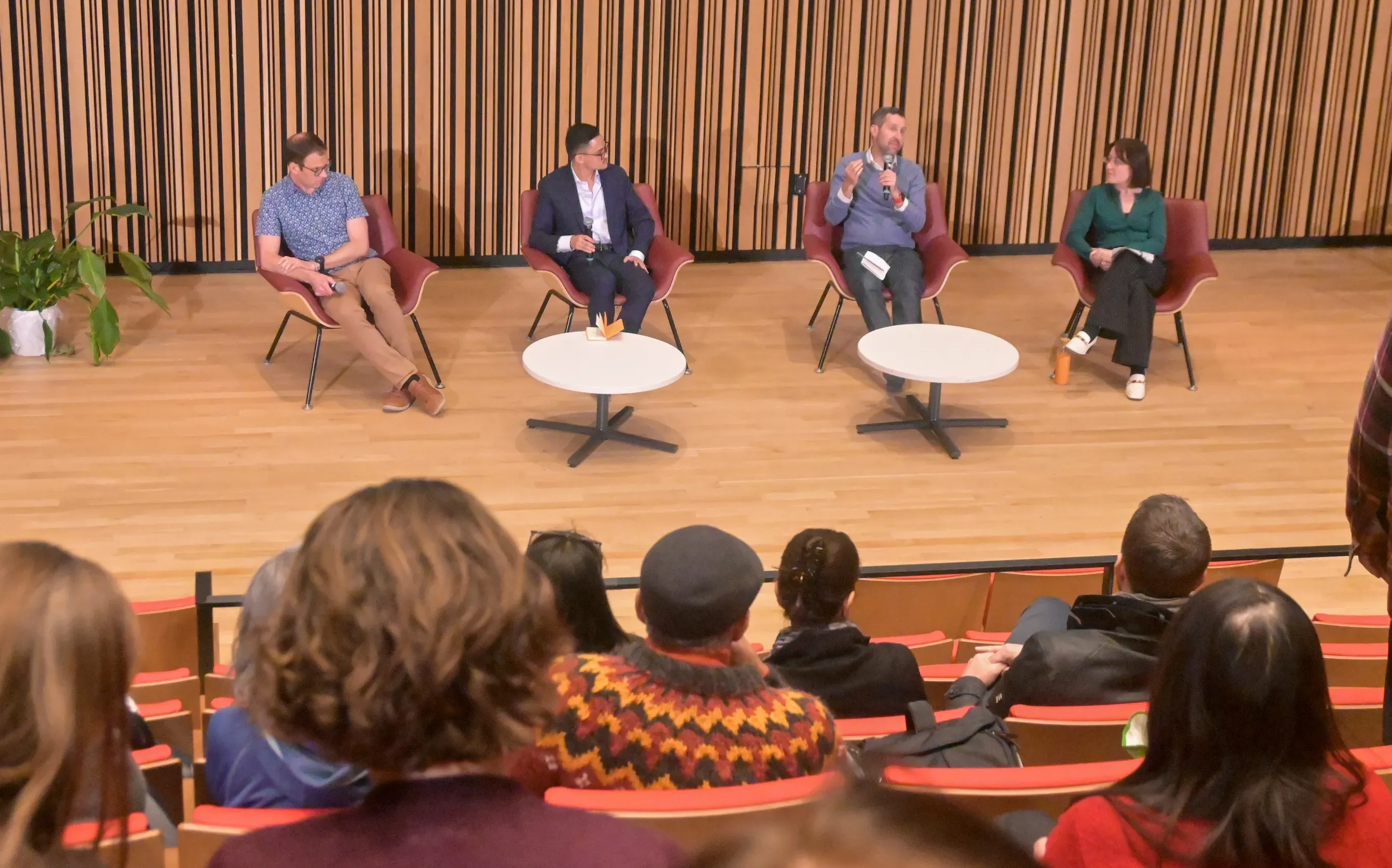 Four panelists sit in chairs, with audience members in the foreground