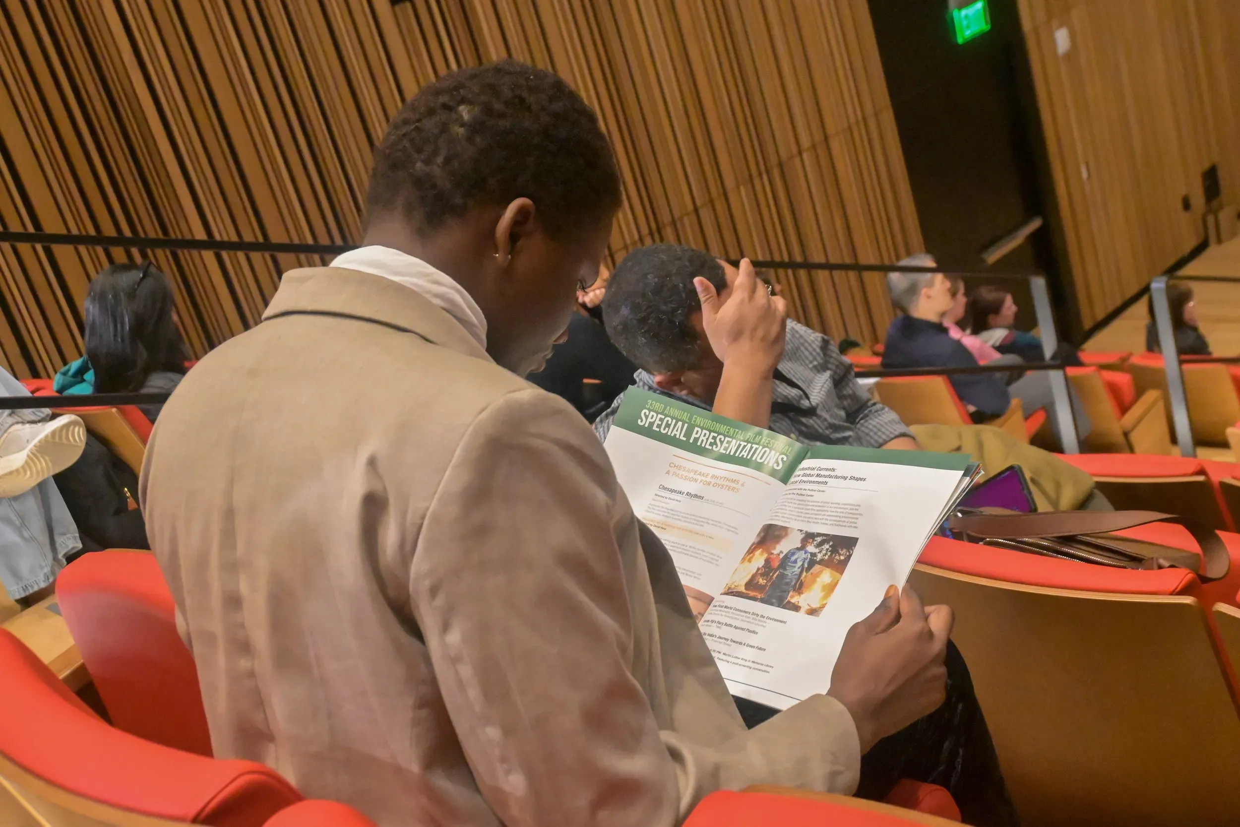 Man in tan jacket looks at event program