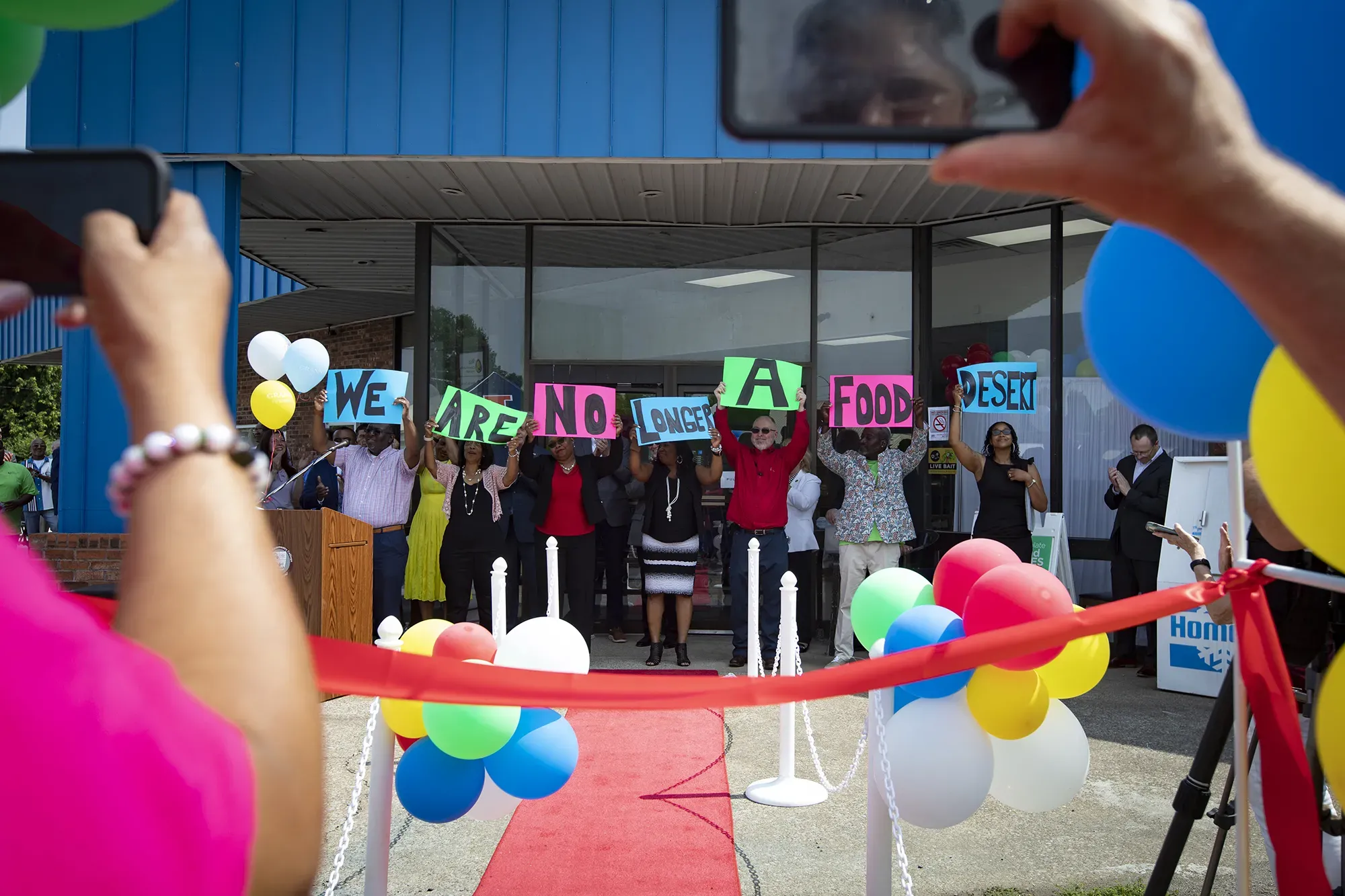 Board members and other stakeholders raise signs reading, “We are no longer a food desert,” at the grand opening of Rise Community Market in Cairo, Illinois
