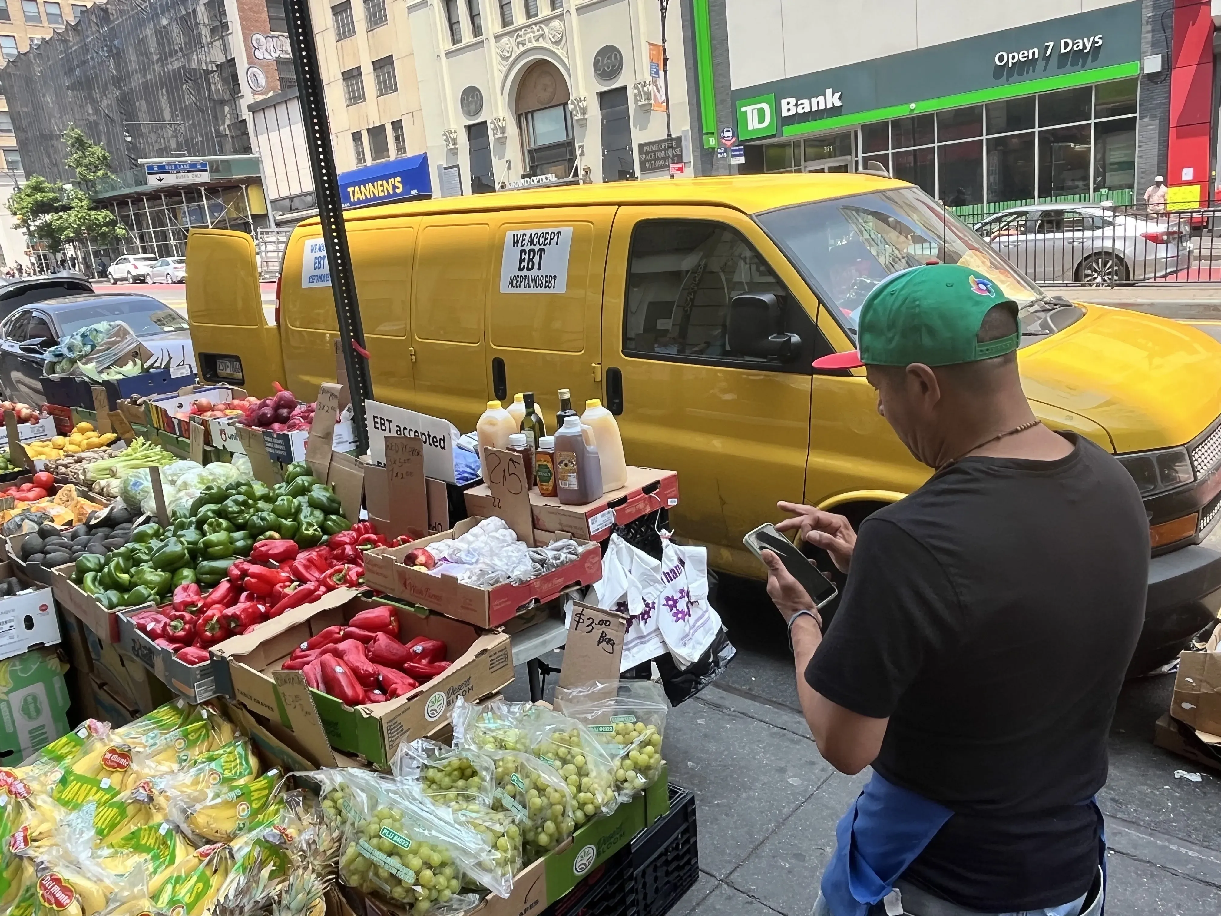Man looks at his phone next to his fruit stand