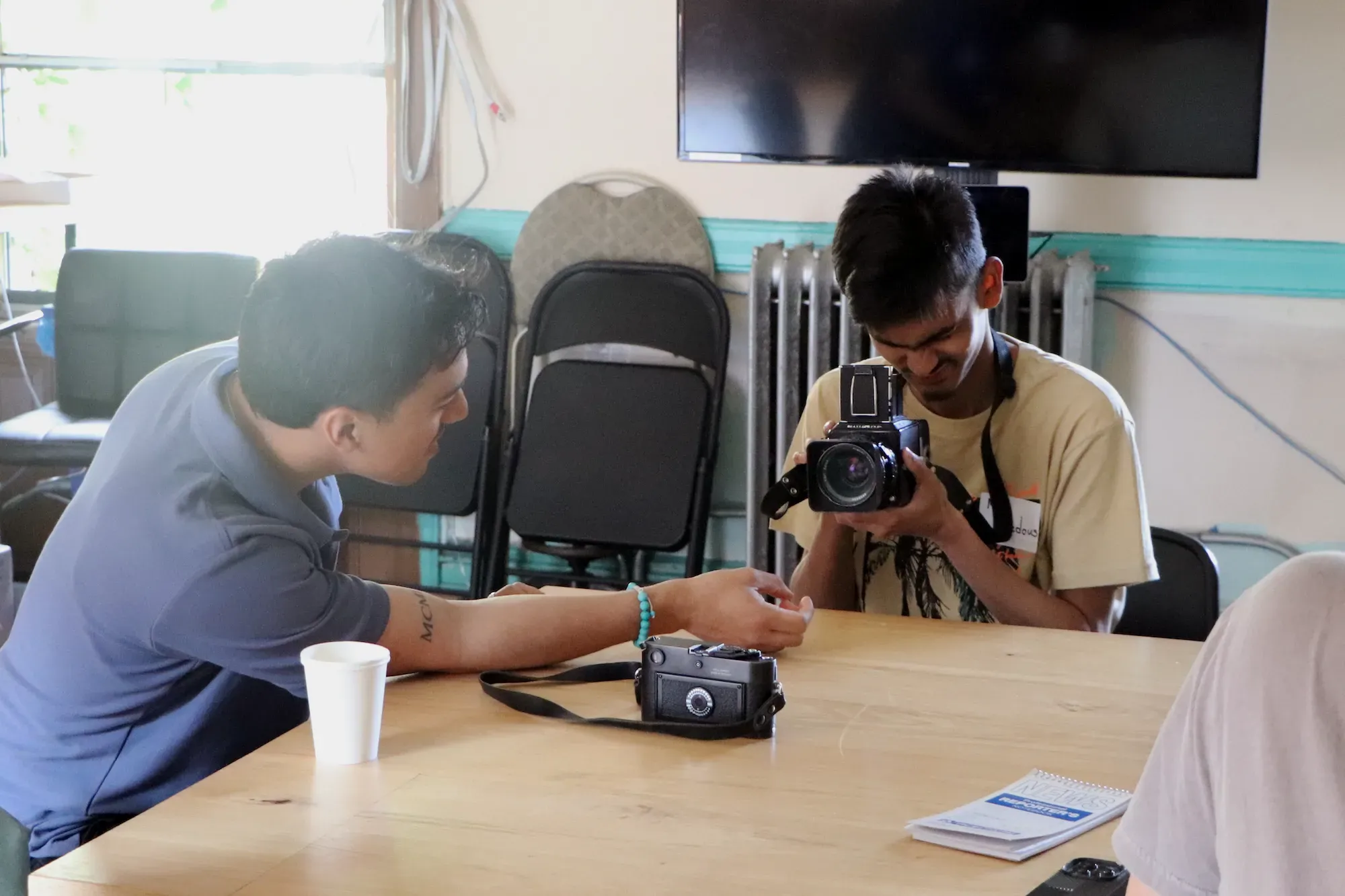 Man in blue shirt shows student in yellow shirt his vintage camera