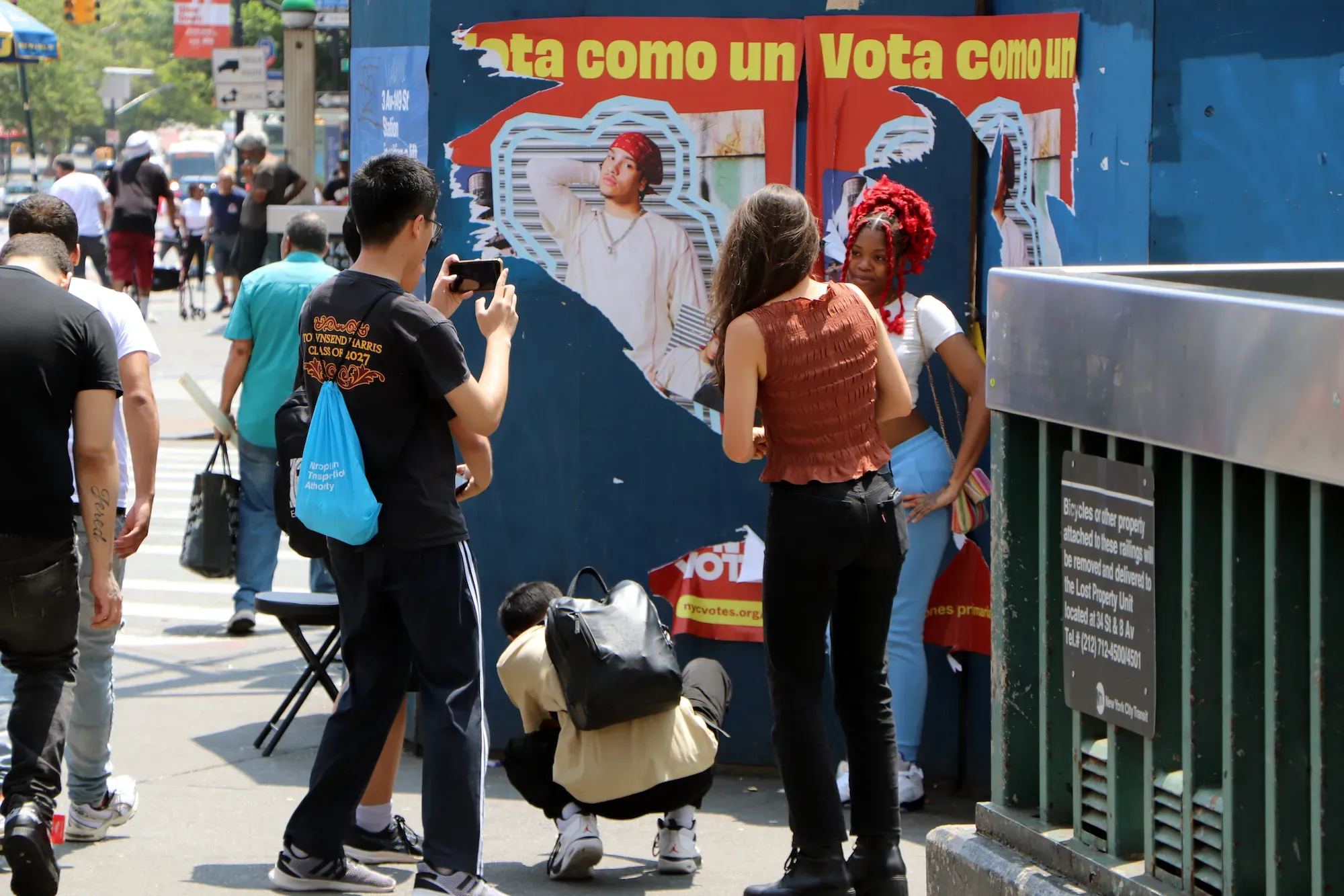 Two students take a photo of a woman posing in front of a poster