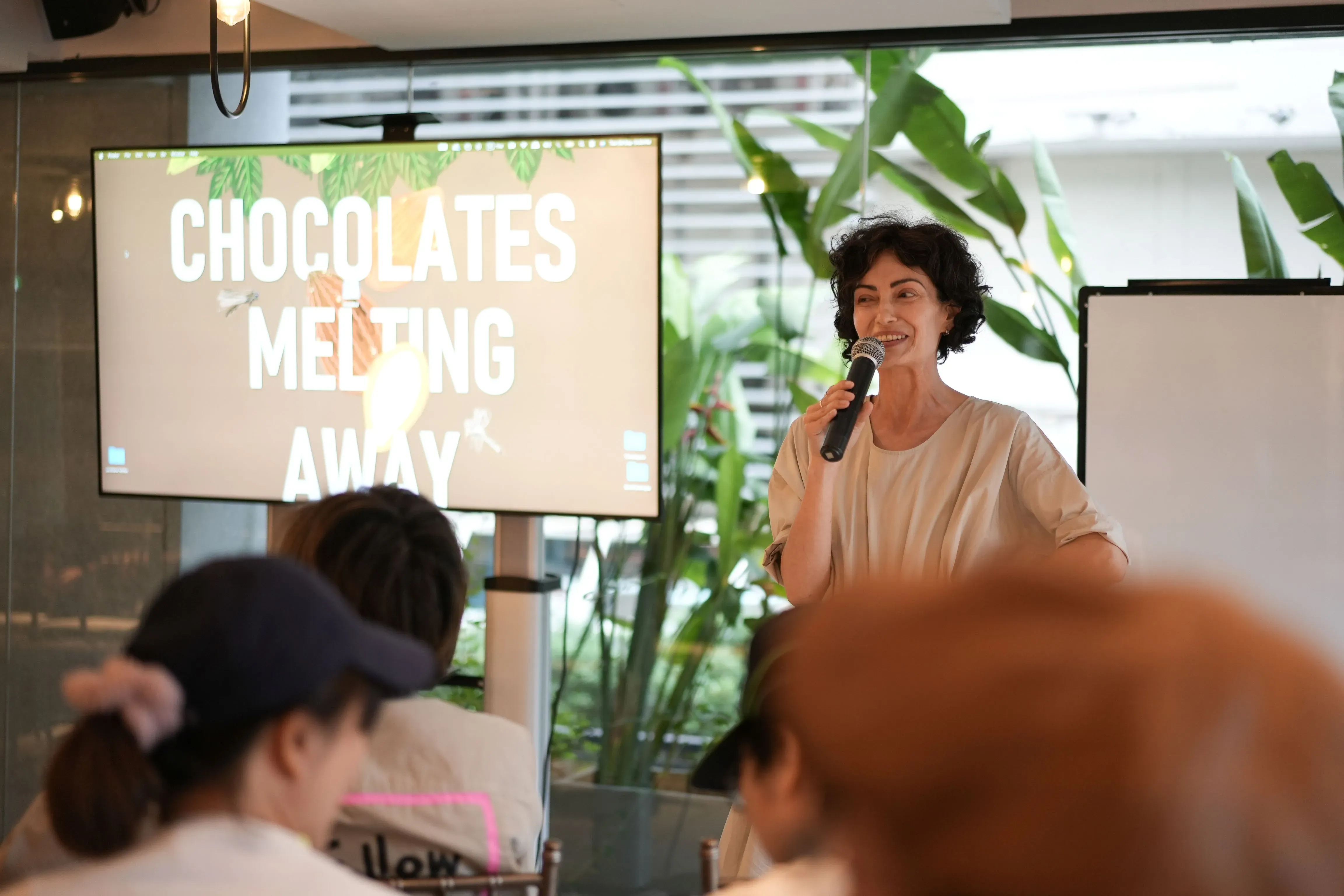 A woman talks into a microphone in front of a projector screen
