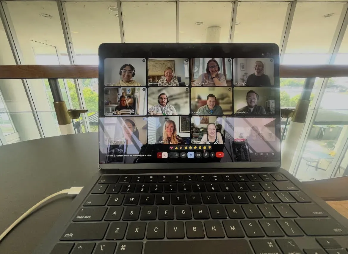 A laptop shows a Zoom call with people smiling on screen