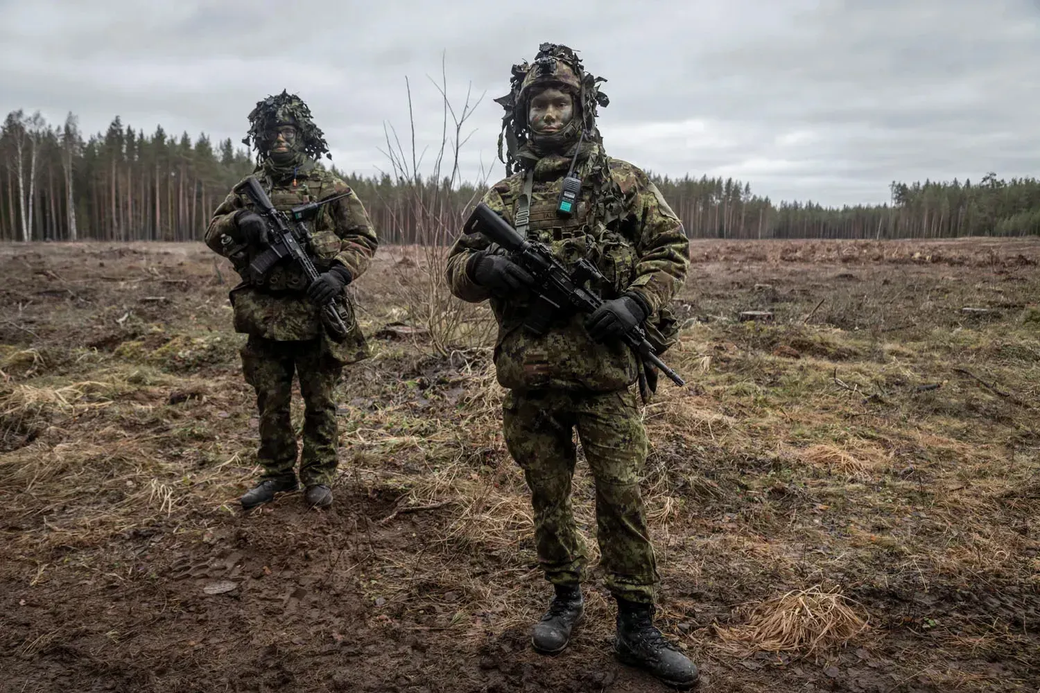 Two young soldiers armed, in uniform with painted faces pose for a picture