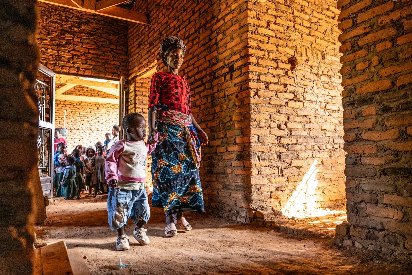 Joyce Chavula and her 3-year-old, Trust, walk through the unfinished health post at Katenje, in central Malawi