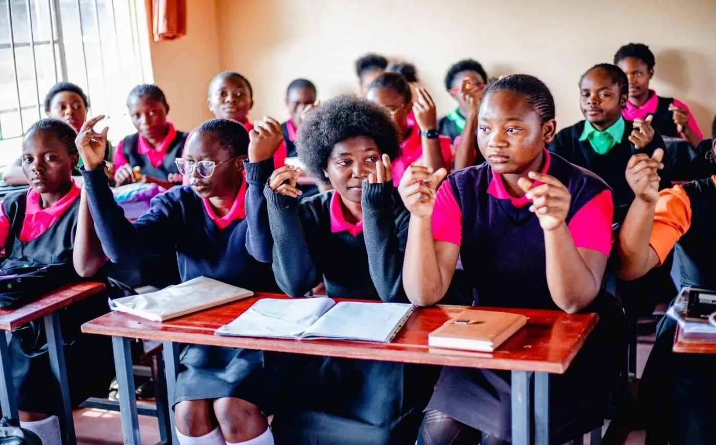 Female students sit in a classroom at their desks, snapping their fingers.