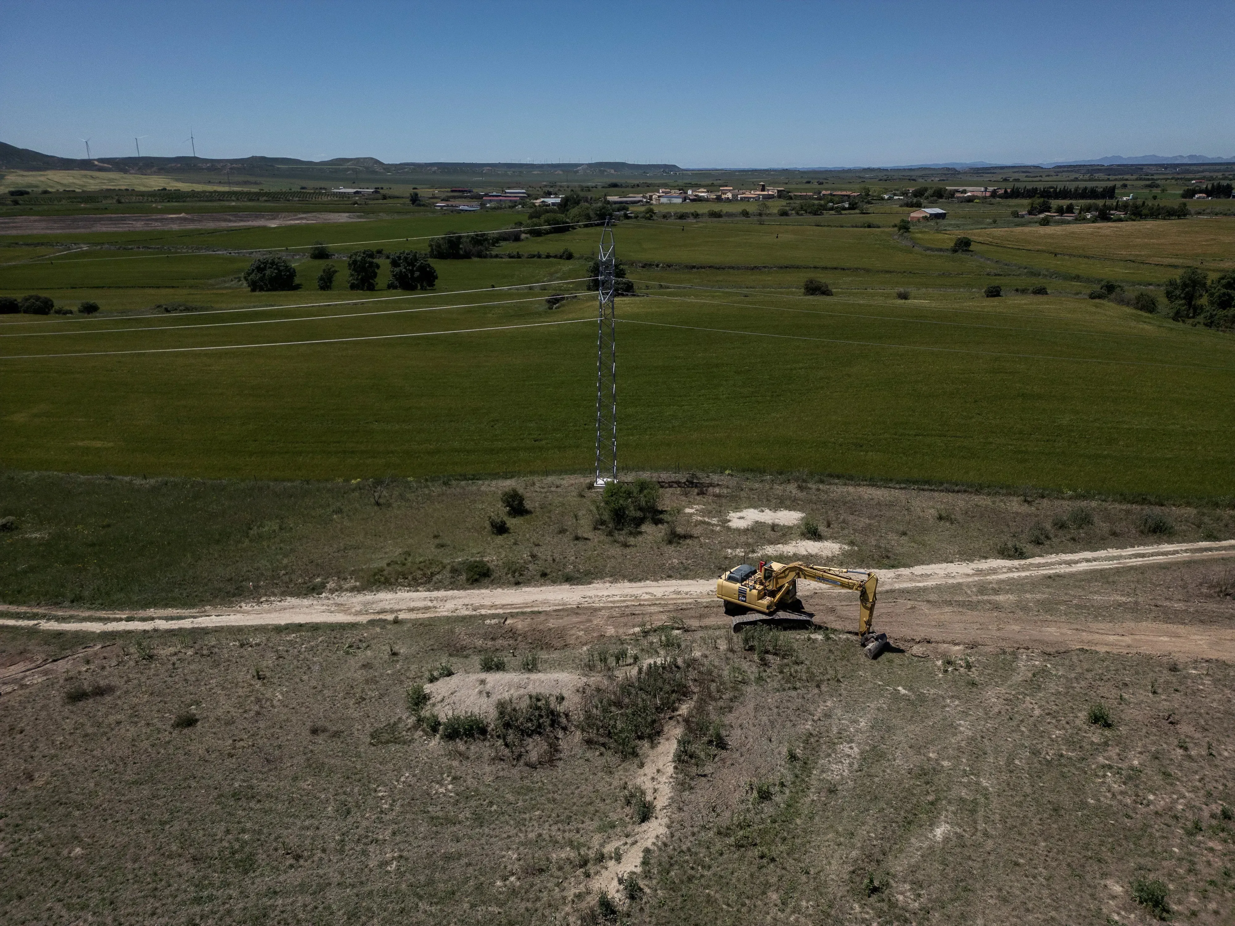 An excavator works on land near the Walqa industrial park in Huesca, where Amazon Web Services (AWS) is building a new data center as part of its expansion plan in Aragón. In the background of the image is the district of Cuarte. Image by Albert Garcia. Spain, 2025.