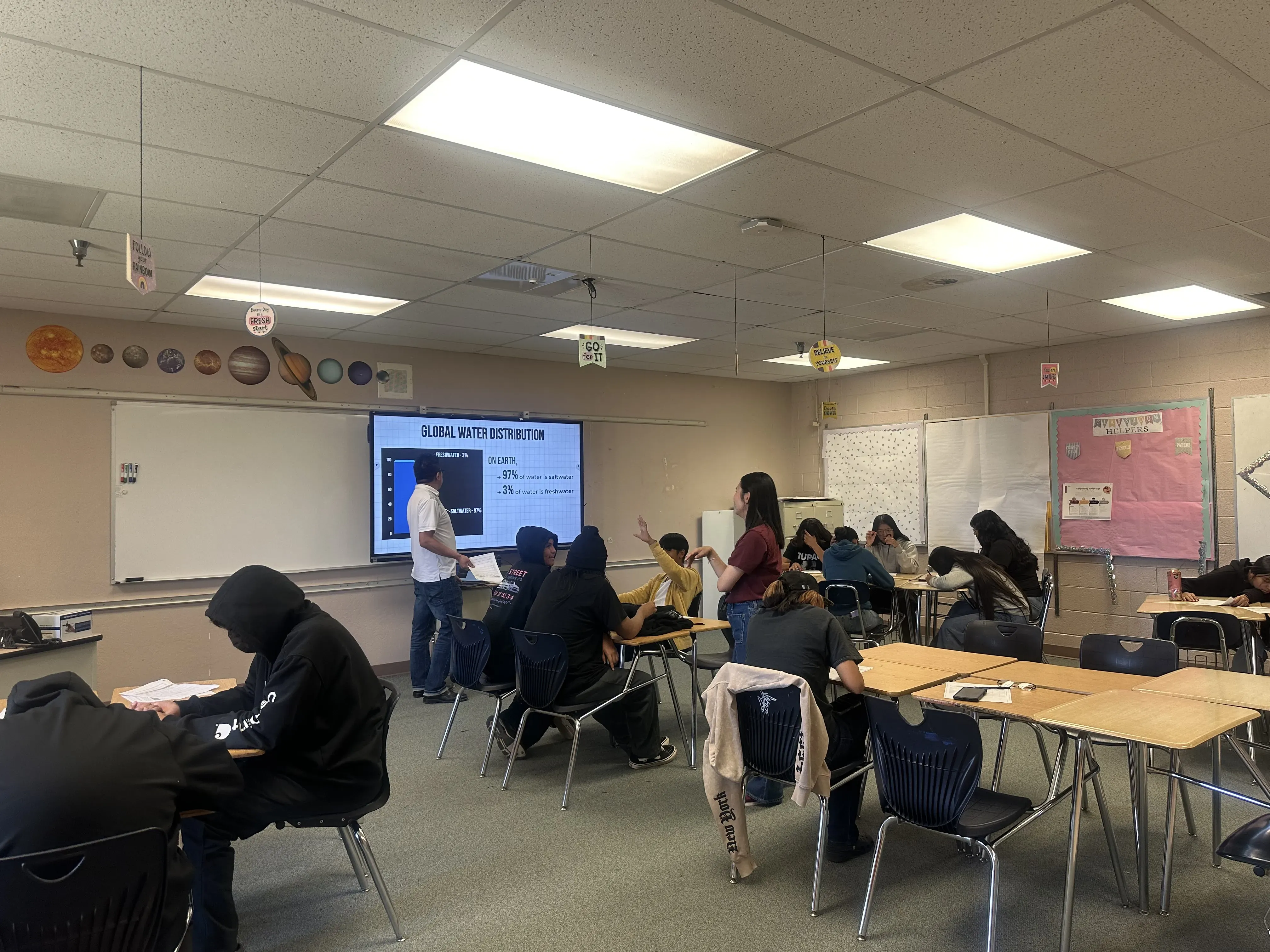 a classroom of students observes teacher giving presentation at smartboard