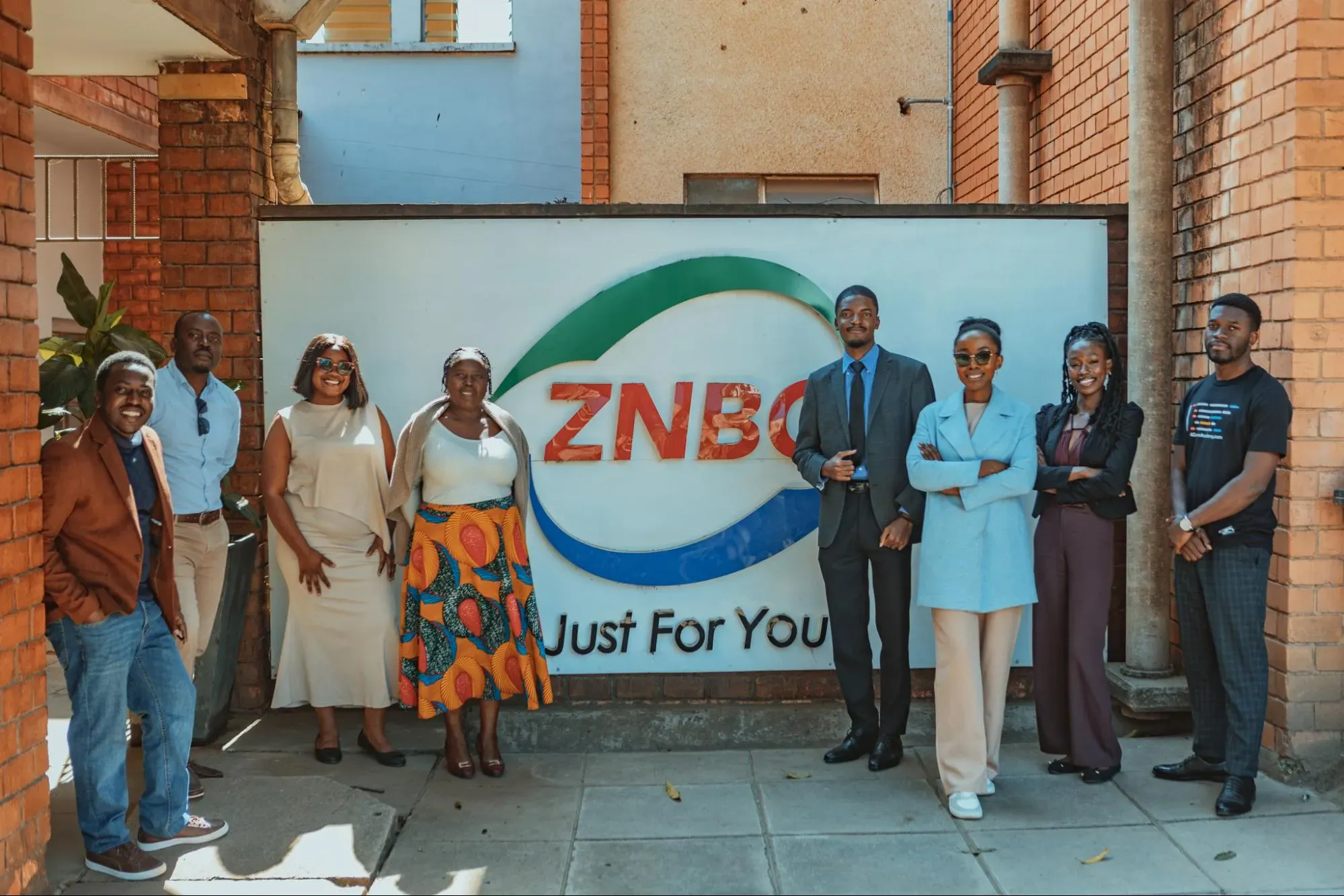 People stand in front of ZNBC sign