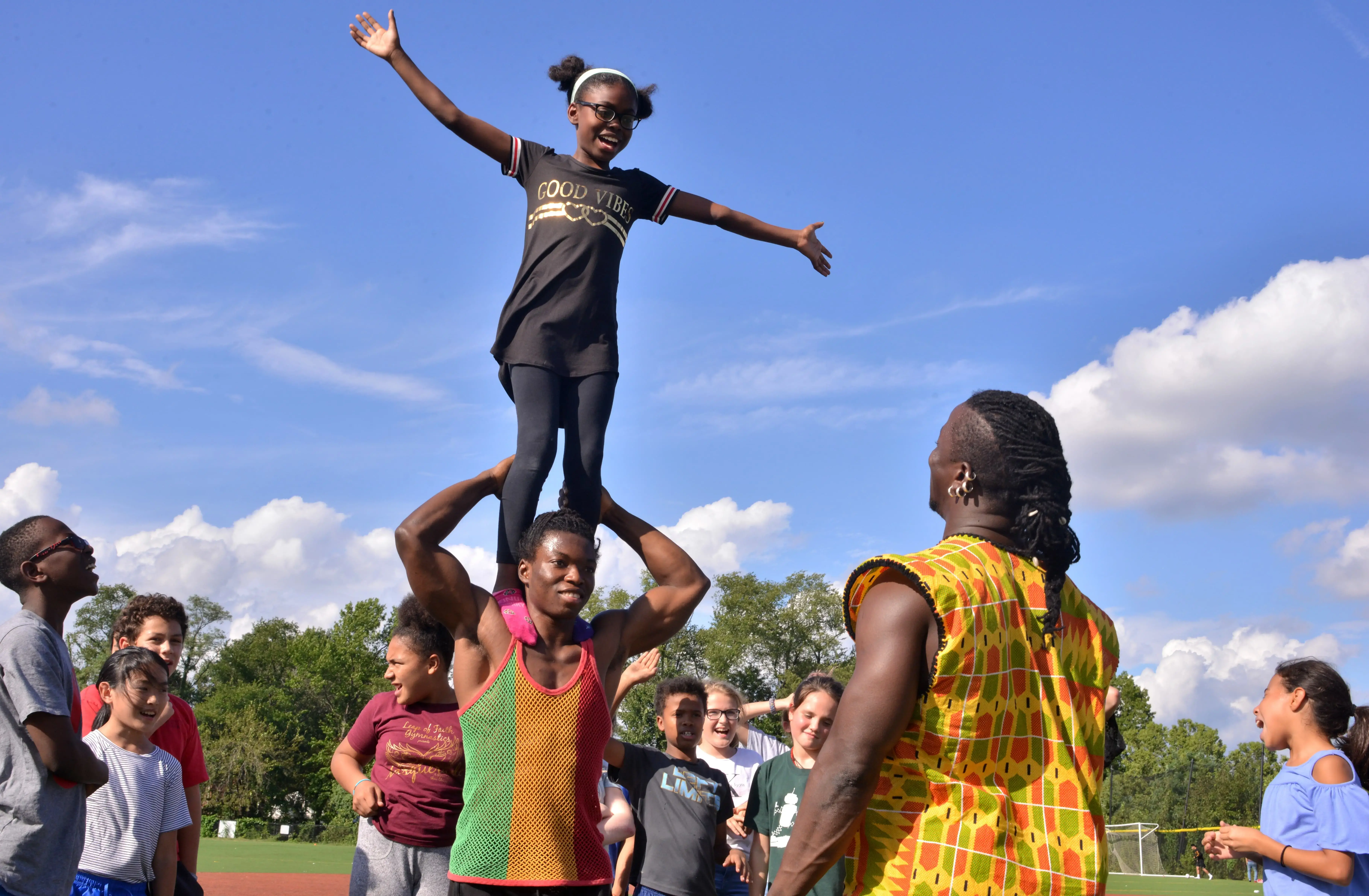 A Deal Middle School sixth grader balances on the shoulders of a Circus Kalabanté acrobat. Image by Dermot Tatlow. United States, 2018. A Deal Middle School sixth grader balances on the shoulders of a Circus Kalabanté acrobat. Image by Dermot Tatlow. United States, 2018.