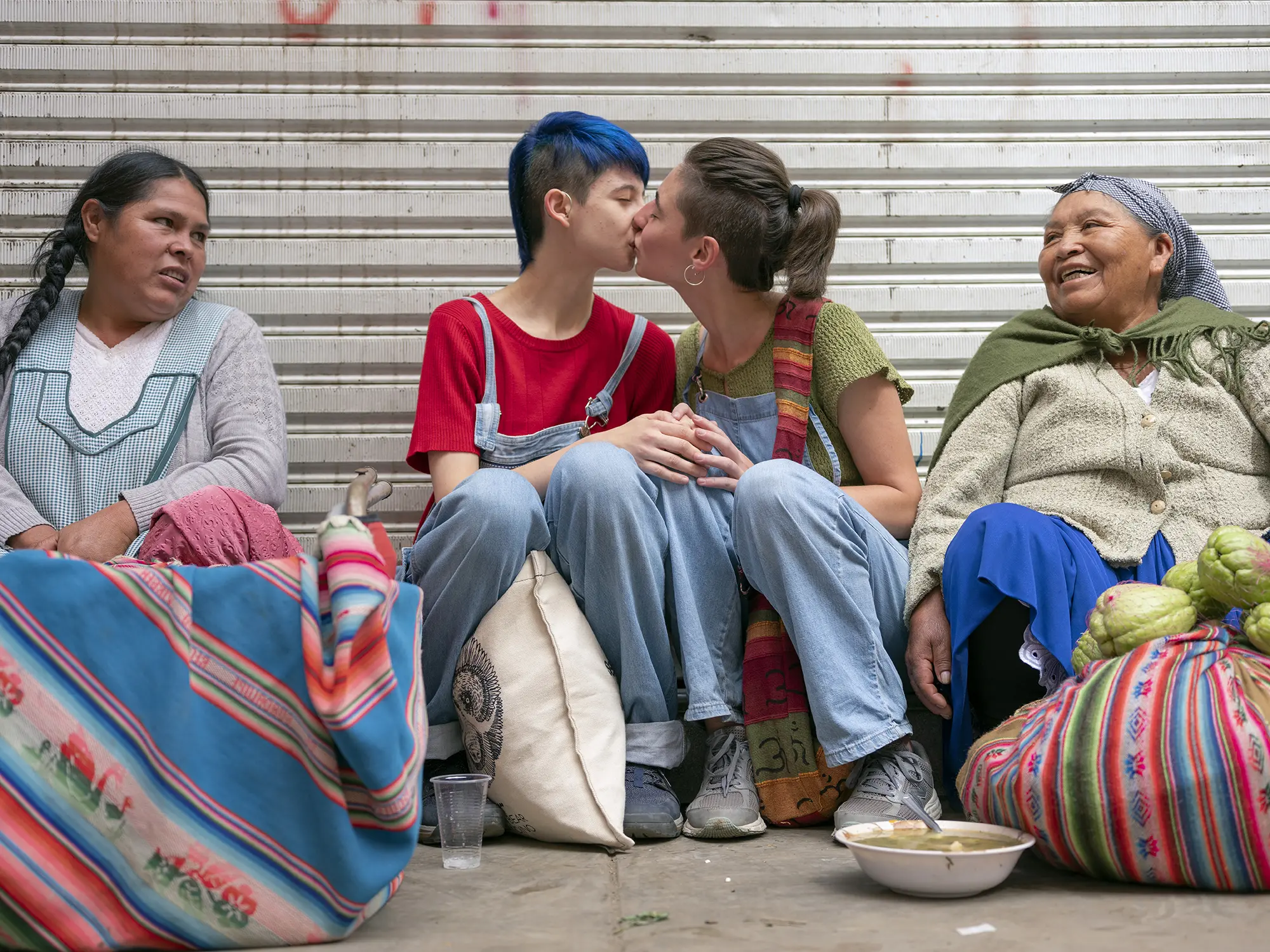 Two people kiss while two women look on smiling