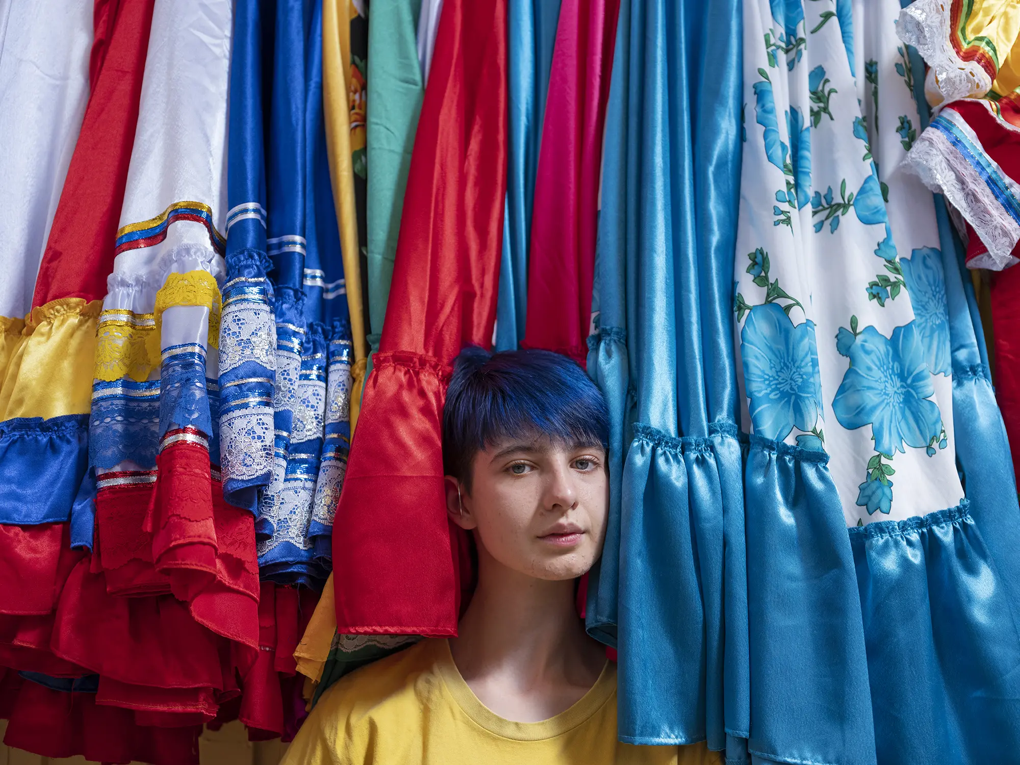 A young individual stands between traditional dresses