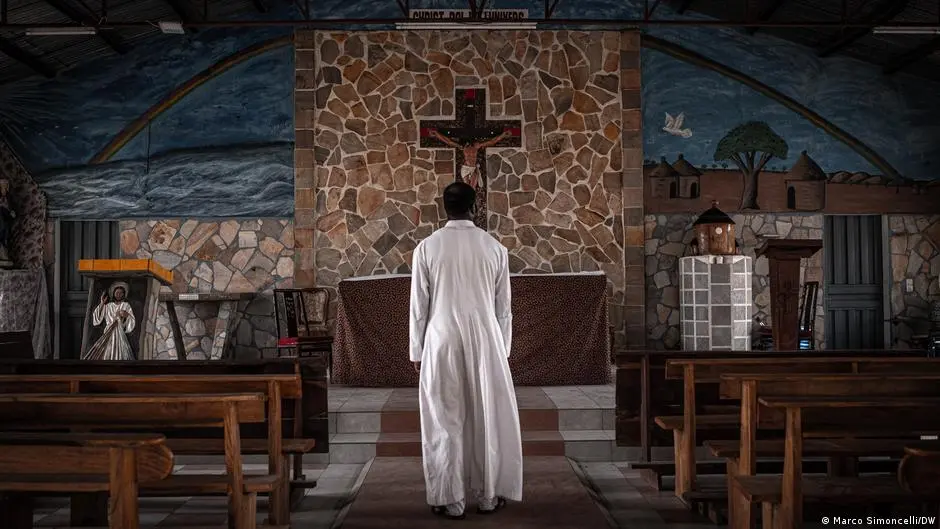 A man faces away from the camera and looks down a church aisle towards the altar.