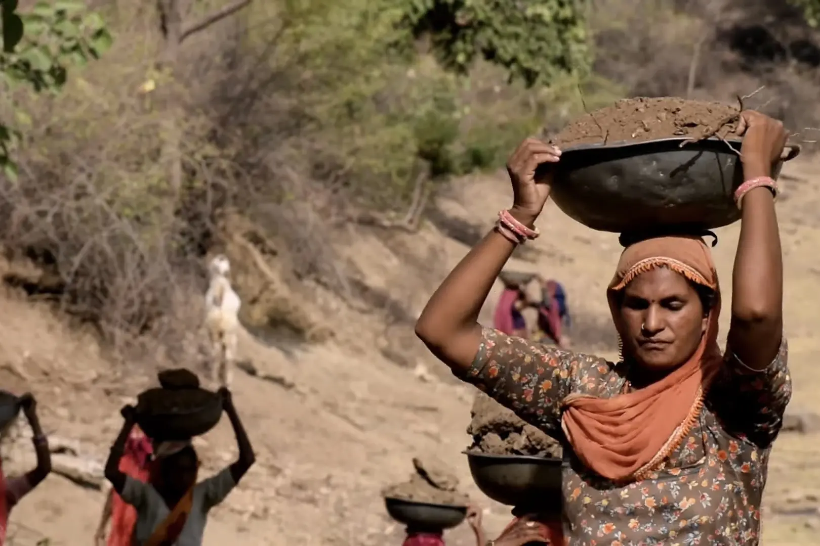 A woman worker holds a bowl full of soil on top of her head.