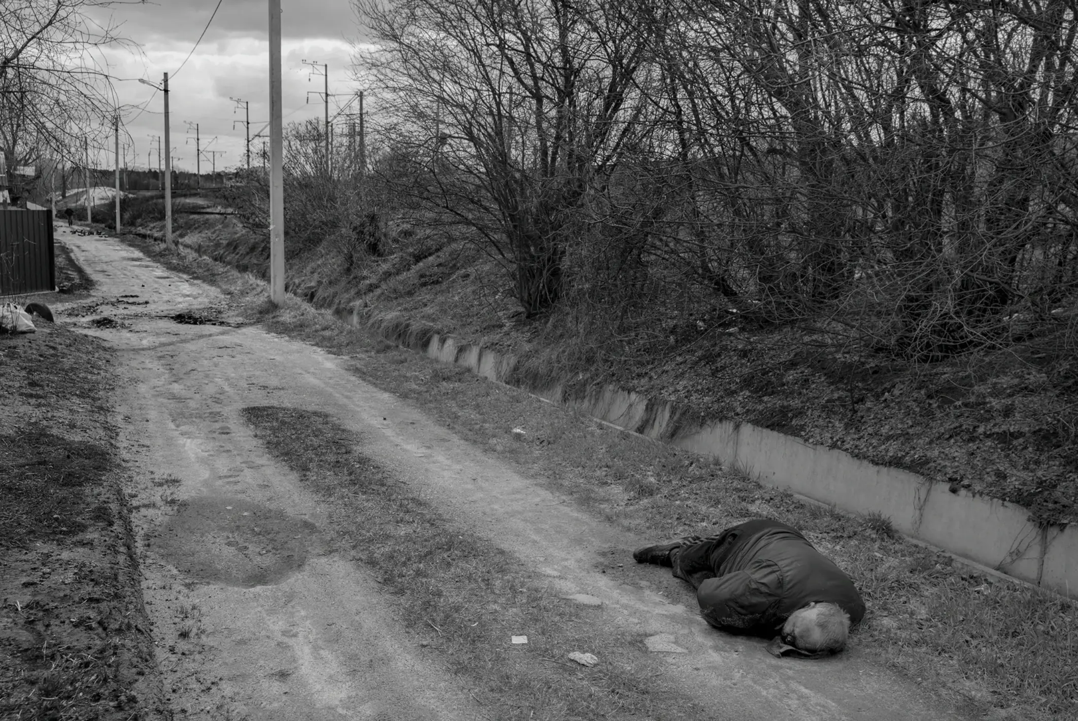 The corpse of a man in civilian clothes lies in a road.