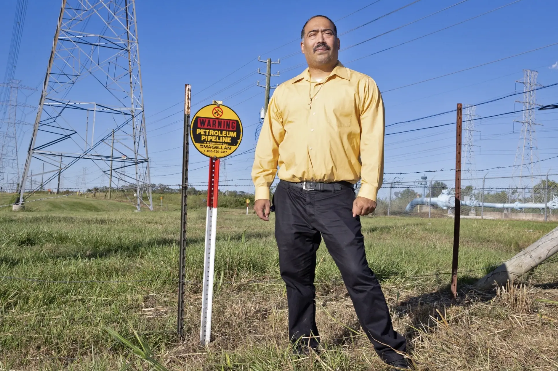 A man stands in front of a pipeline in his hometown next to a warning sign that indicates their pipeline
